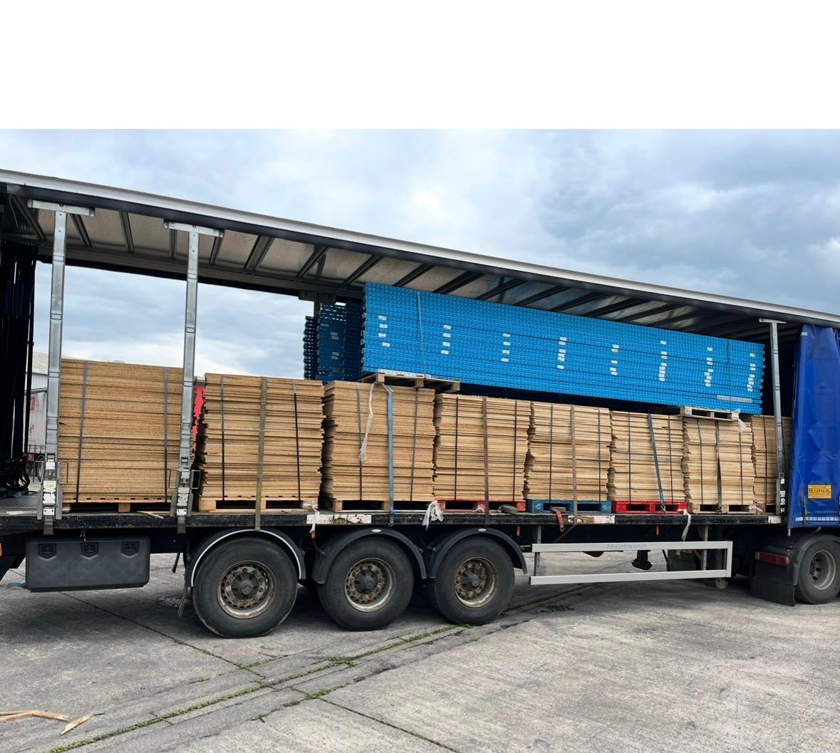A curtain-side trailer loaded with mezzanine decking boards and blue steel beams
