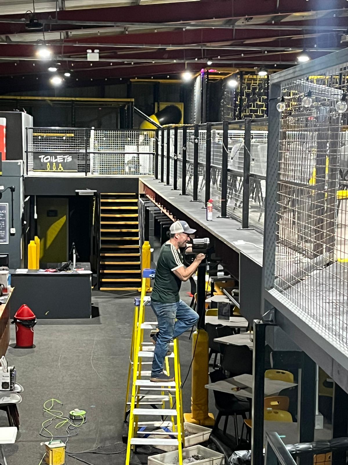 An installer fitting handrail posts to a mezzanine edge in a leisure venue