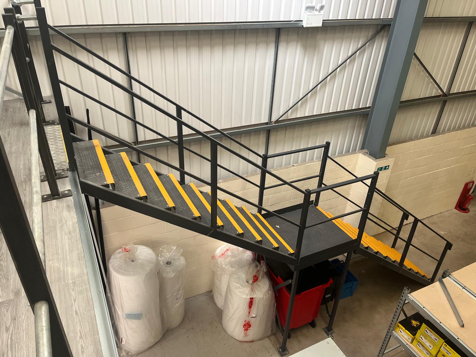 Black steel mezzanine staircase with yellow step nosings and a half landing