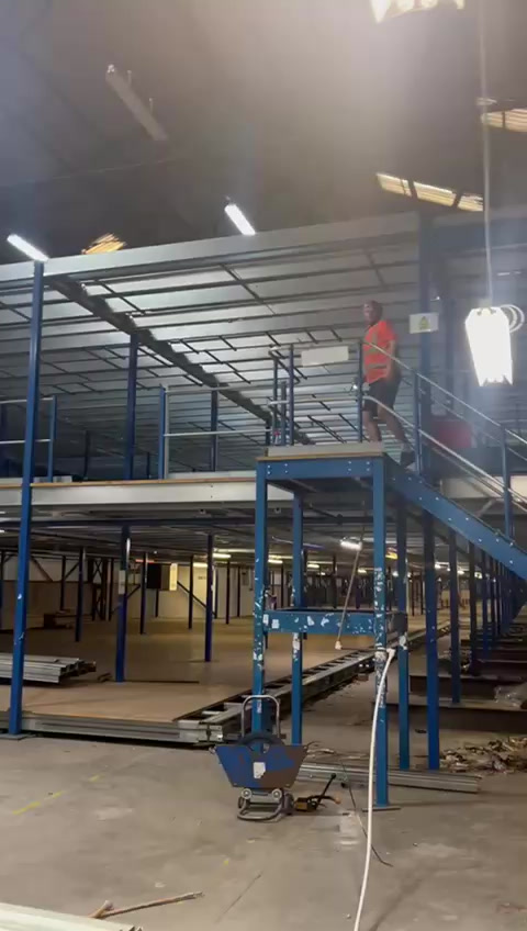A two-tier blue steel mezzanine under construction in a large warehouse